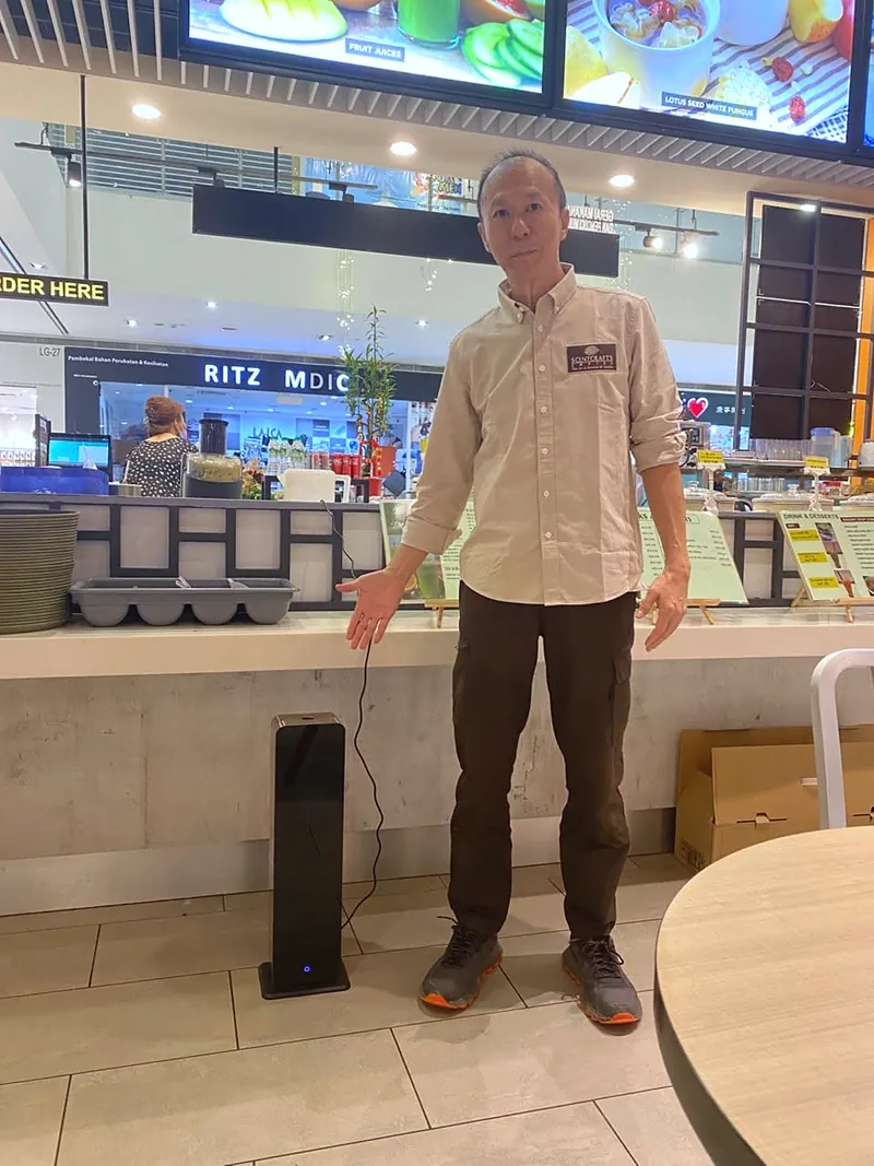 Valent Yeong, Scent Up's partner in Malaysia, beside a black tower scent diffuser in a shopping centre food court in Malaysia.